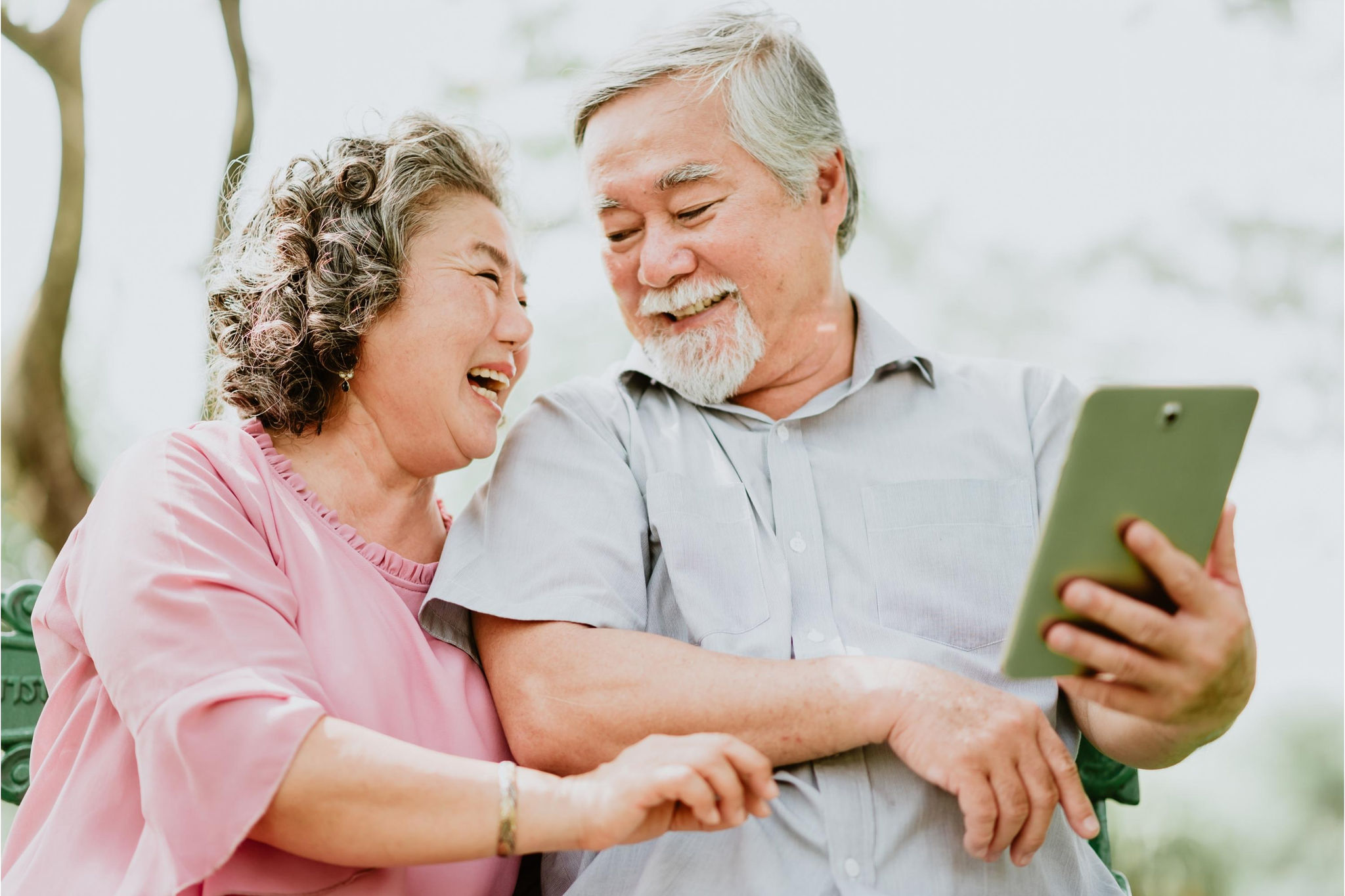 canva-senior-couple-laughing-tablet-outdoors