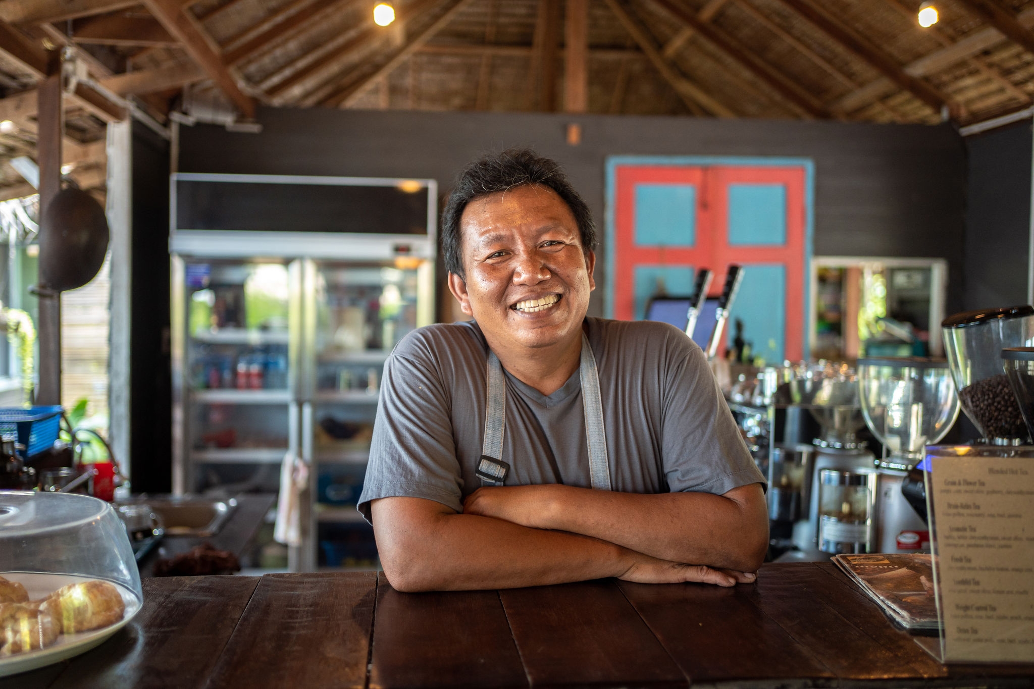 Smiling man is standing at the bar counter and looking at camera in a coffee shop.
