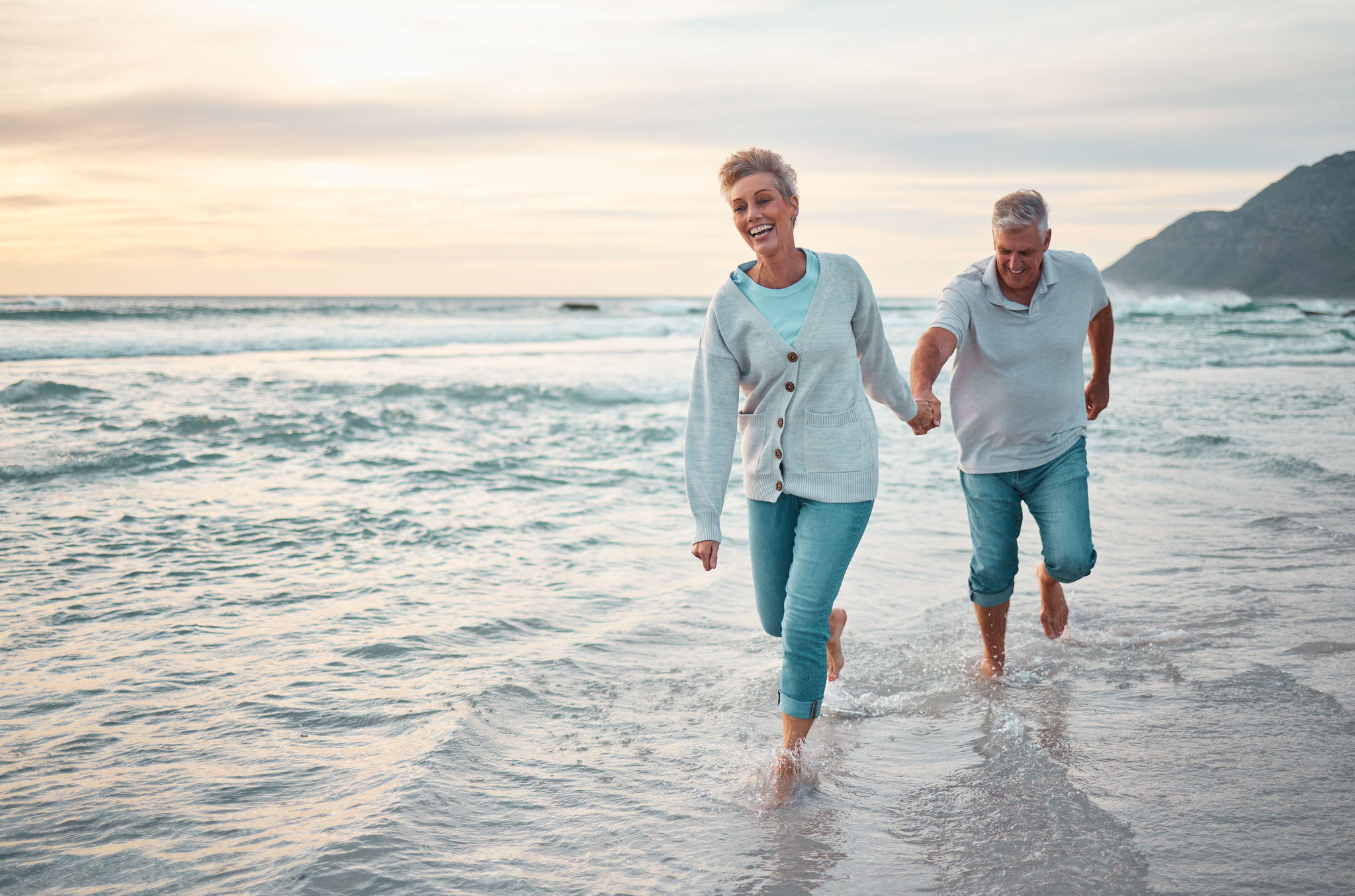 Beach, walking and senior couple holding hands for support, love and care with outdoor wellness, retirement and holiday lifestyle with sunset sky. Elderly people running together in sea ocean water.