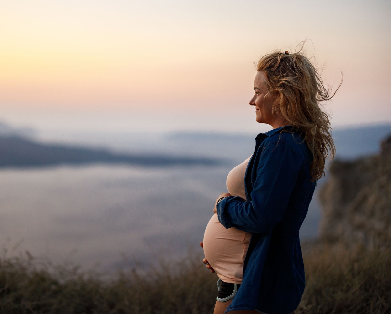 Smiling pregnant woman day dreaming during summer vacation on a hill above the sea. Copy space.